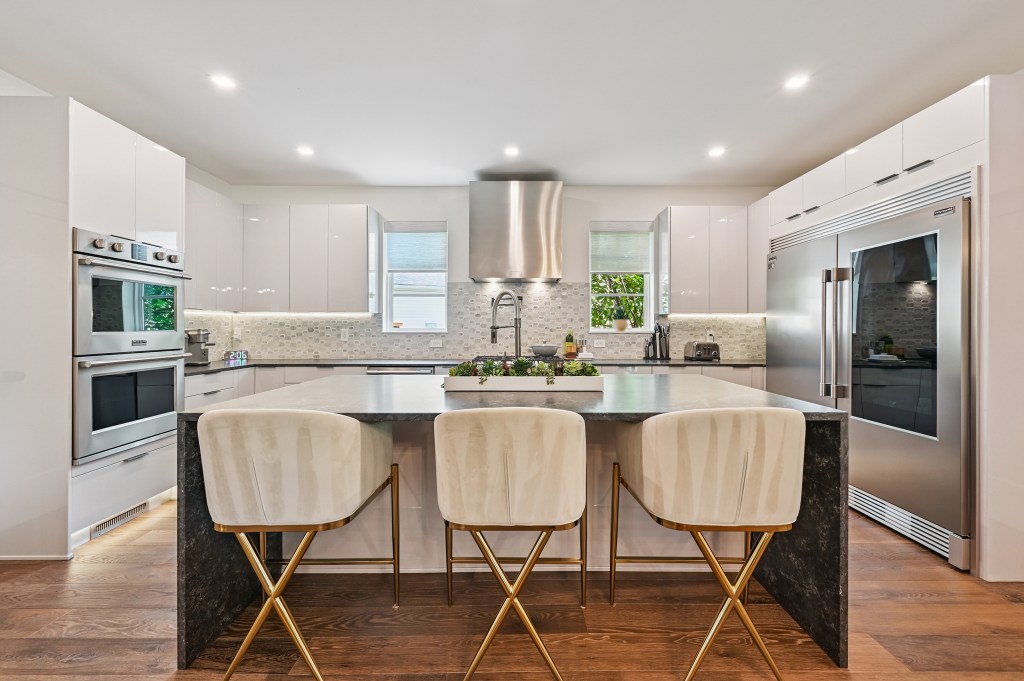 A contemporary kitchen with a central island, stainless steel appliances, and natural wood flooring.