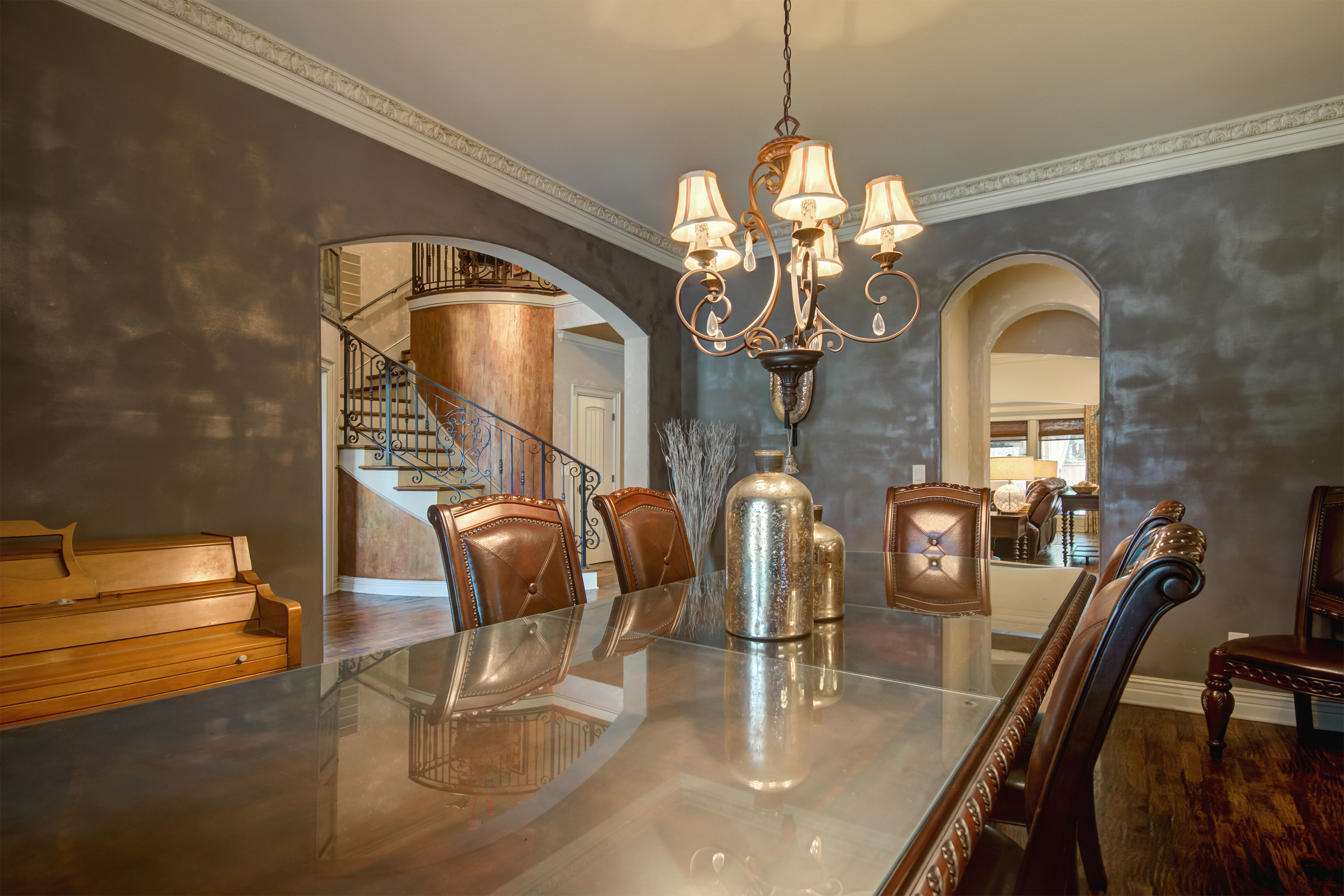 A dining room with a large, rectangular glass table and six leather chairs. Three archways are seen. The one to the right ...